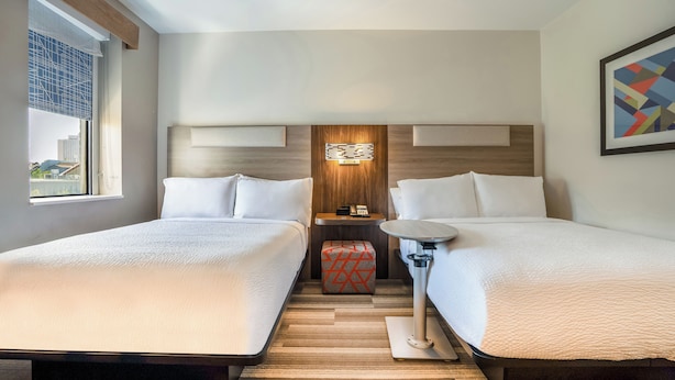 A hotel room with two beds, a small table, a nightstand, and a window with a view of buildings. - Holiday Inn Express New Orleans - Arts District by IHG (New Orleans)