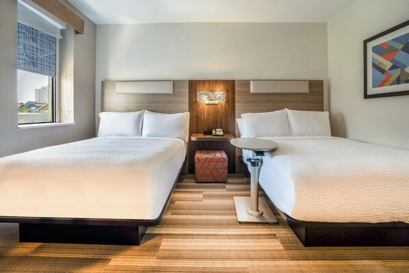 A hotel room with two beds, a small table, a nightstand, and a window with a view of buildings. - Holiday Inn Express New Orleans - Arts District by IHG (New Orleans)