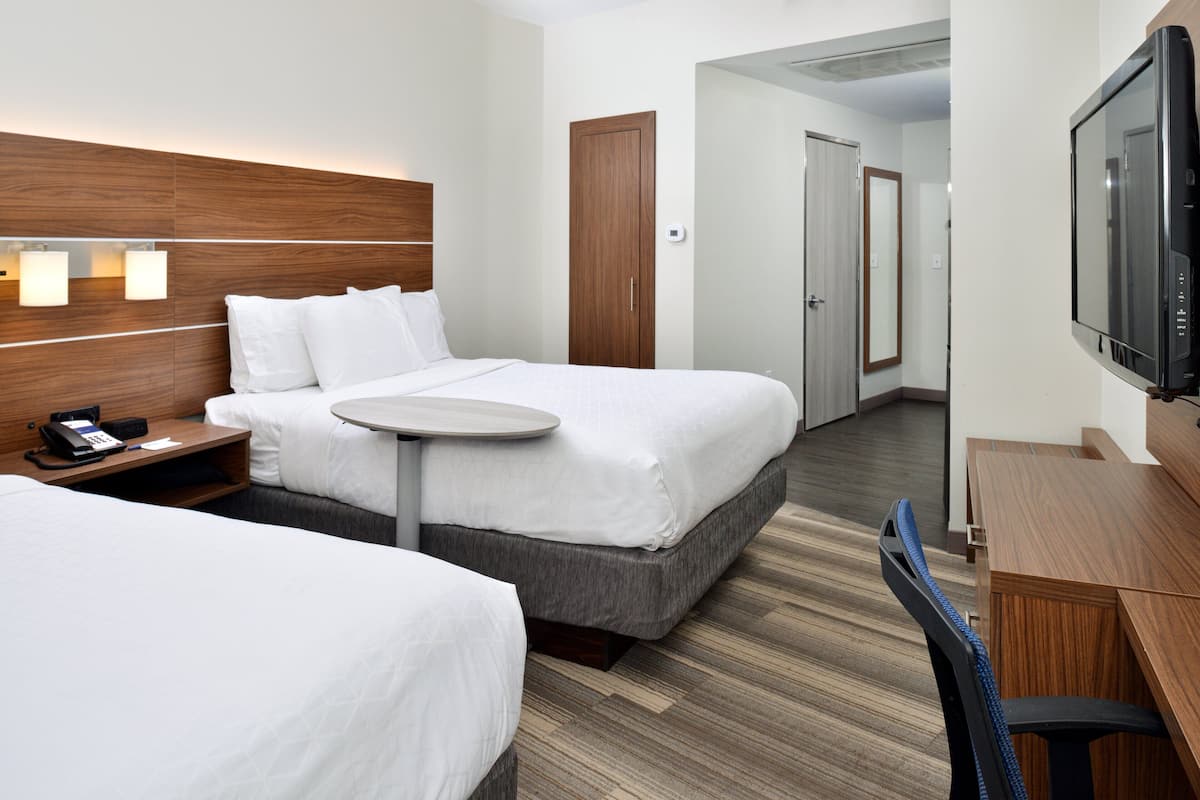A hotel room with two beds, a desk, a chair, a TV, and a door leading to another room.