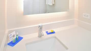 Une salle de bain avec un lavabo blanc, un miroir et des articles de toilette posés sur un tapis bleu.