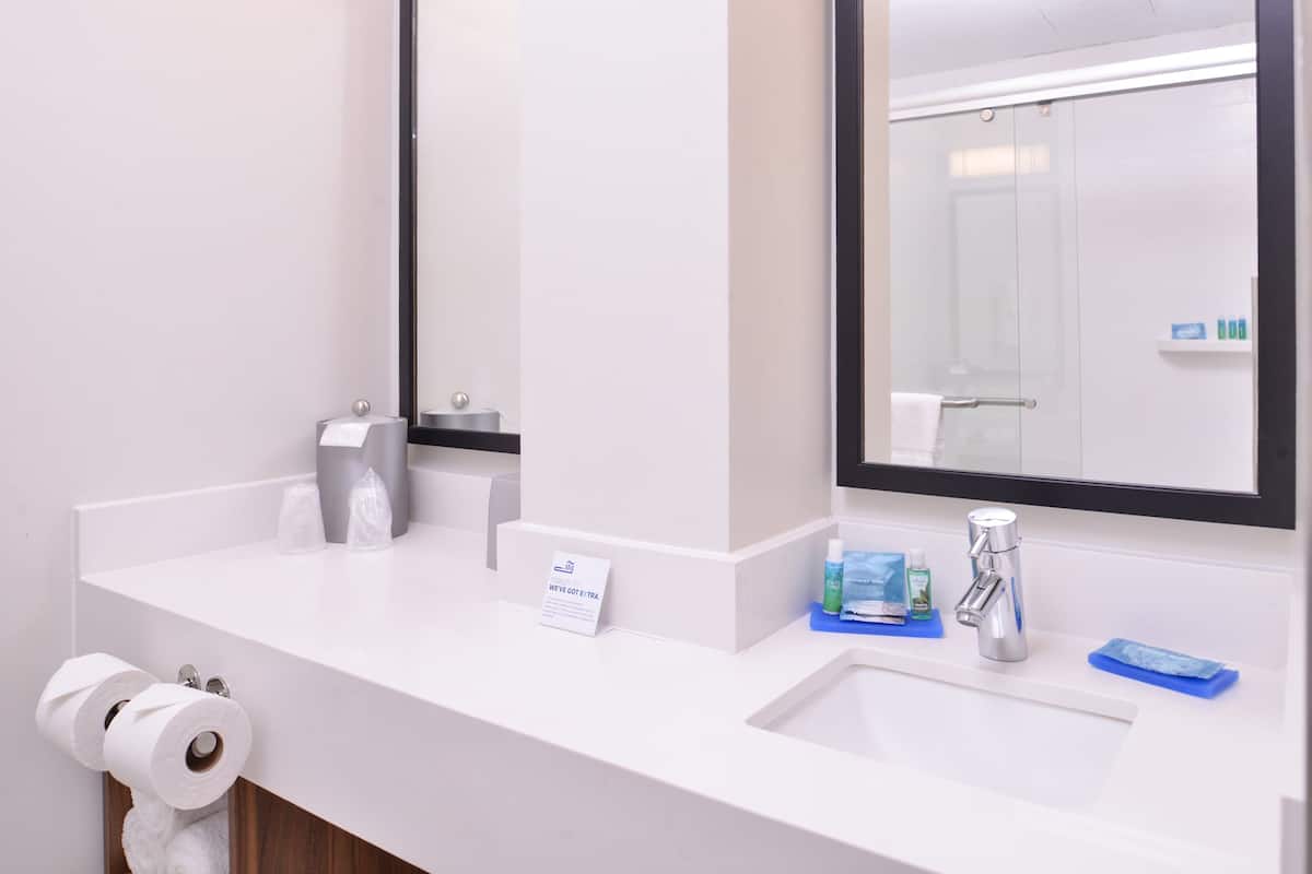 A modern bathroom with a white sink, a mirror, and toiletries.
