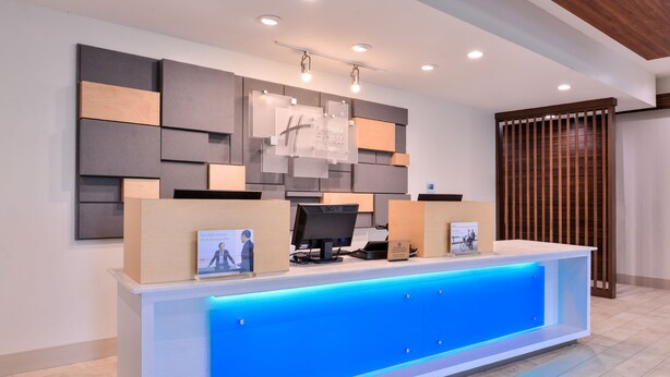 A reception desk with a blue illuminated panel, a flat-screen monitor, and a framed sign above. - Holiday Inn Express New Orleans - Arts District by IHG (New Orleans)