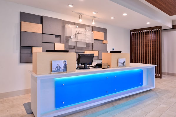 A reception desk with a blue illuminated panel, a flat-screen monitor, and a framed sign above. - Holiday Inn Express New Orleans - Arts District by IHG (New Orleans)