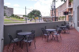 An outdoor patio with tables and chairs, a tram in the background, and a building across the street.