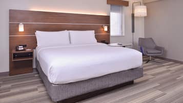 Una habitación de hotel con una cama grande, mesitas de noche, una silla y un ventanal.