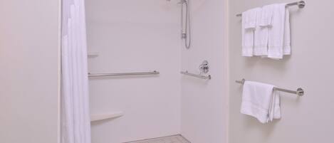 Ducha con barra de apoyo, toallero con toallas y piso de baldosas.