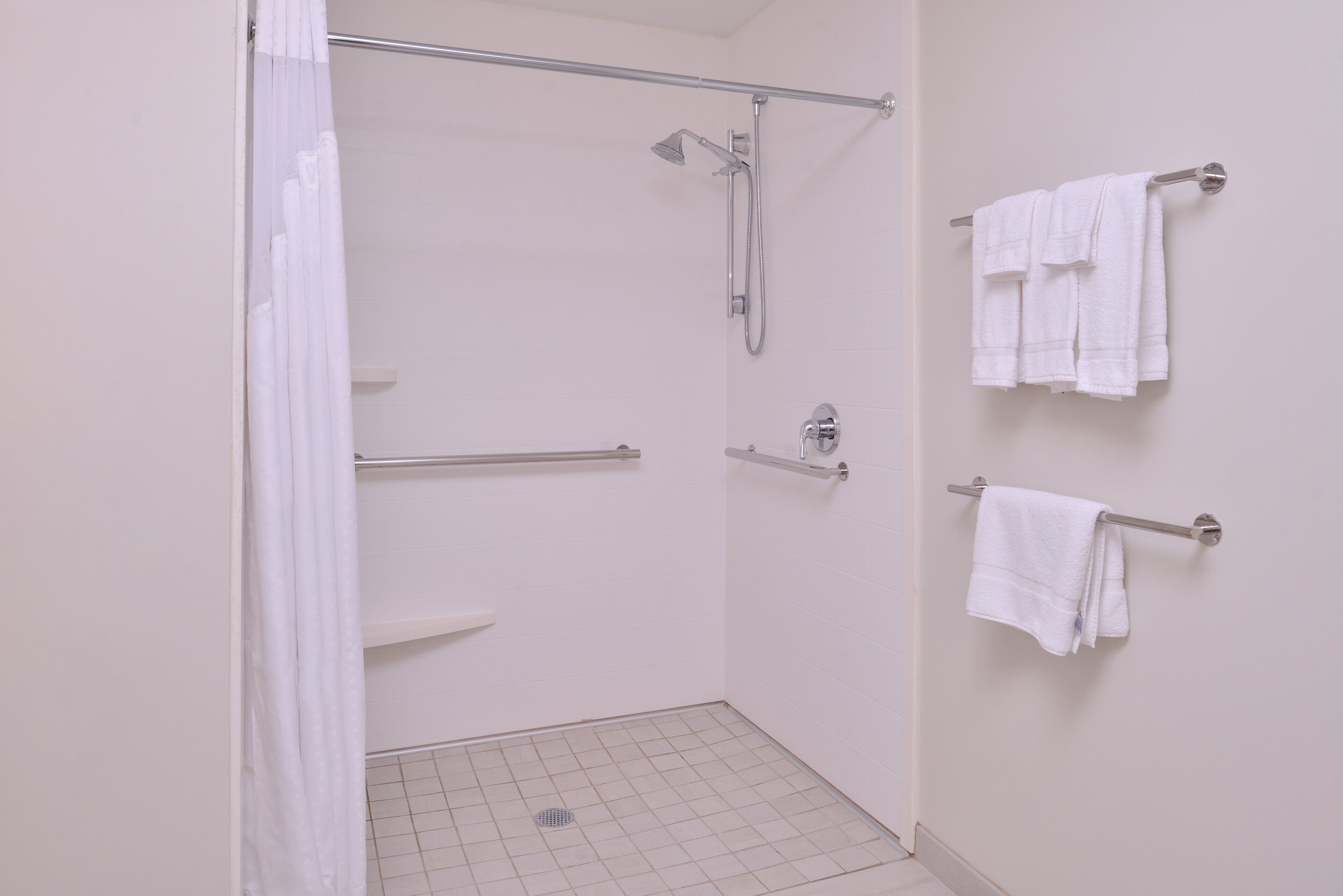 A shower with a grab bar, a towel rack with towels, and a tiled floor.