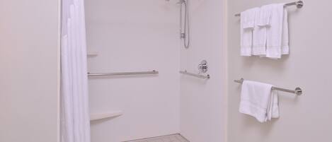 A shower with a grab bar, a towel rack with towels, and a tiled floor.