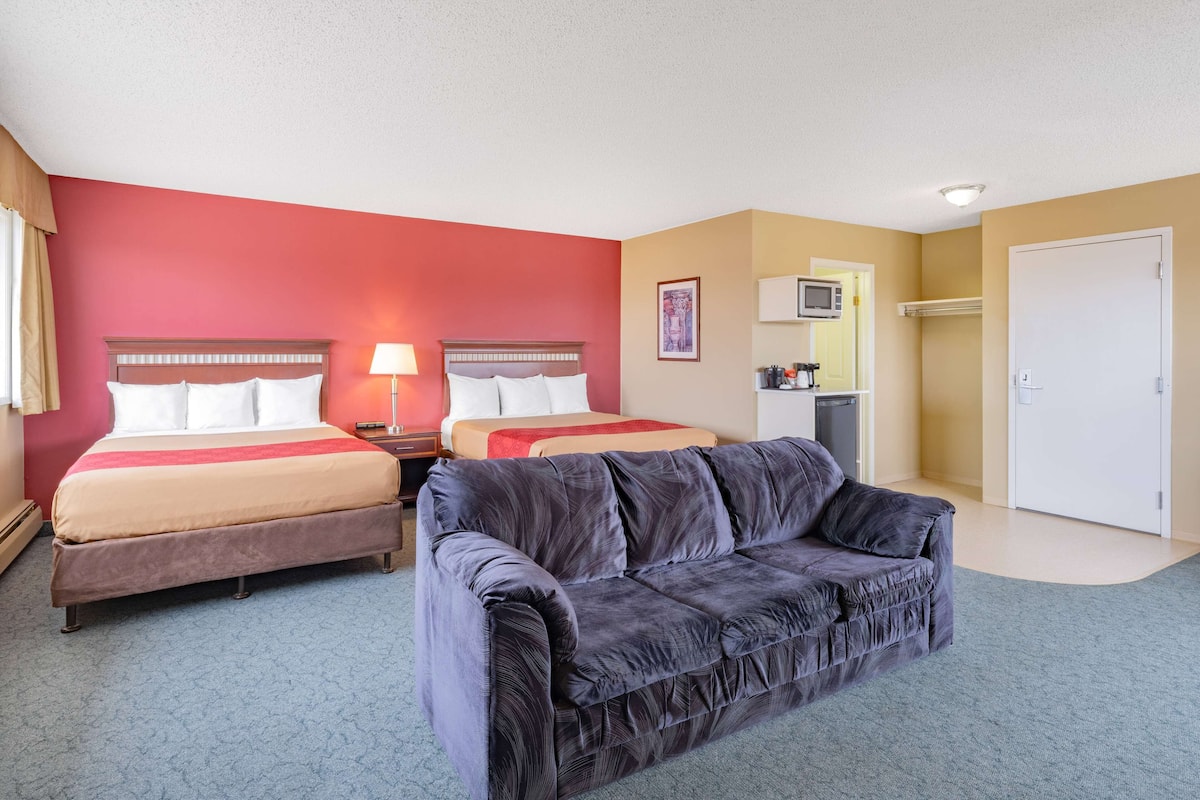 Una habitación de hotel con dos camas, un sofá gris, un microondas y una puerta.