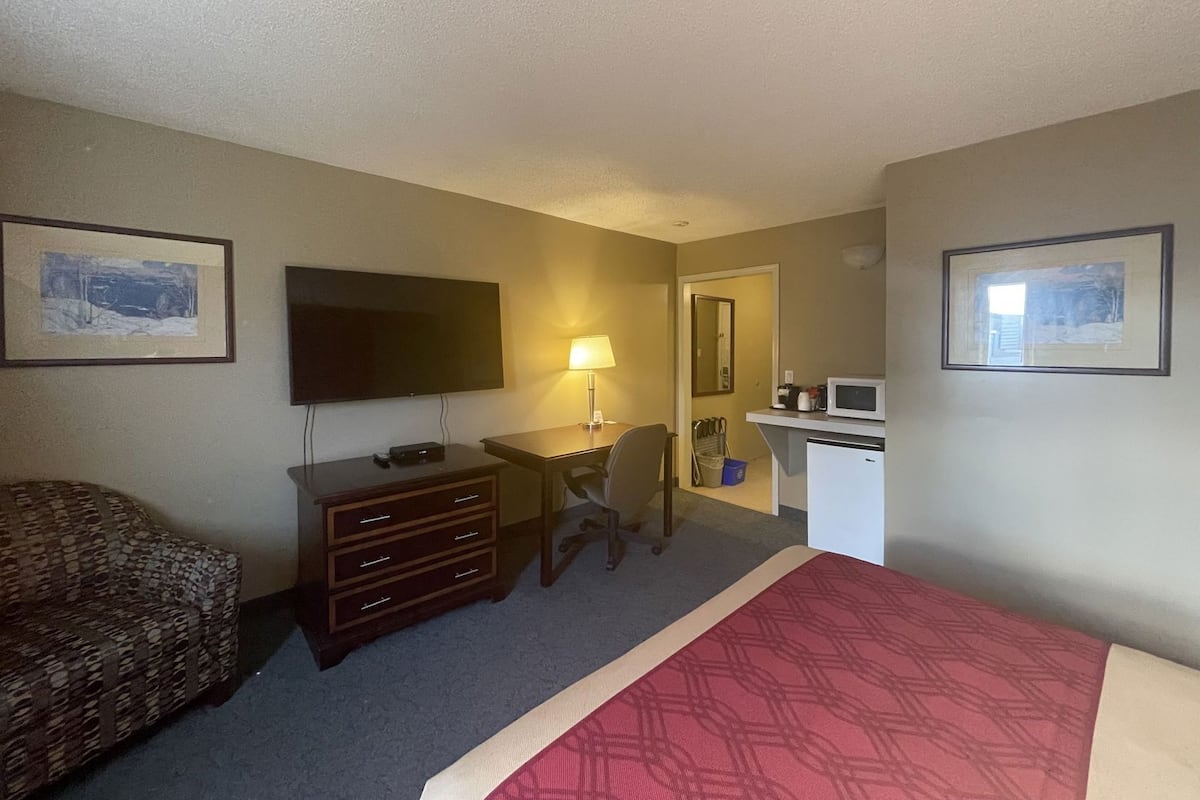 Habitación de hotel con cama, escritorio con silla, televisión, lámpara, microondas y cómoda.