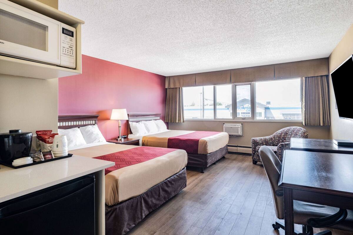 Habitación de hotel con dos camas, un escritorio, una silla, un televisor, una cafetera y una ventana con vistas.