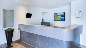A reception area with a modern counter, a mounted TV, a framed certificate, and a large landscape painting.