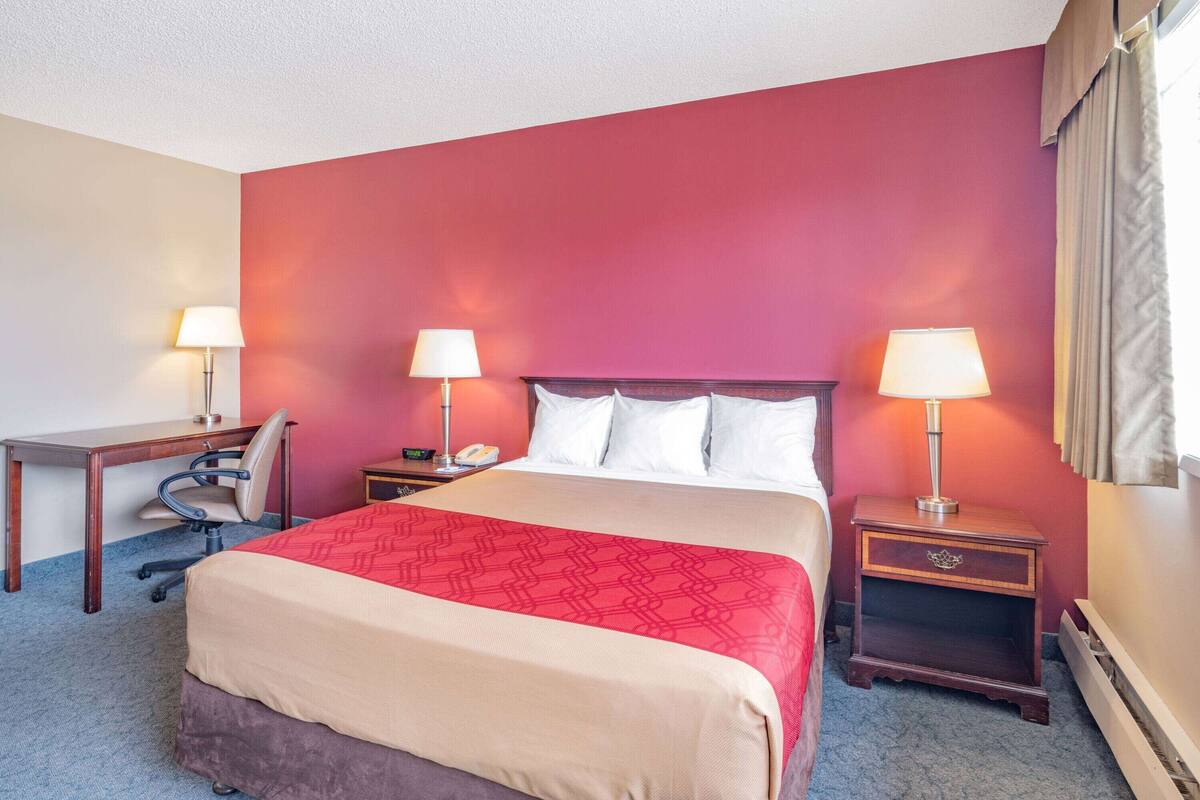 Una habitación de hotel con una cama, dos mesitas de noche con lámparas, un escritorio y una silla.