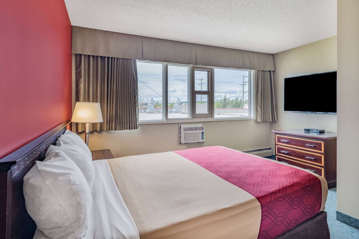 Habitación de hotel con cama, televisión, cómoda y ventana con cortinas.