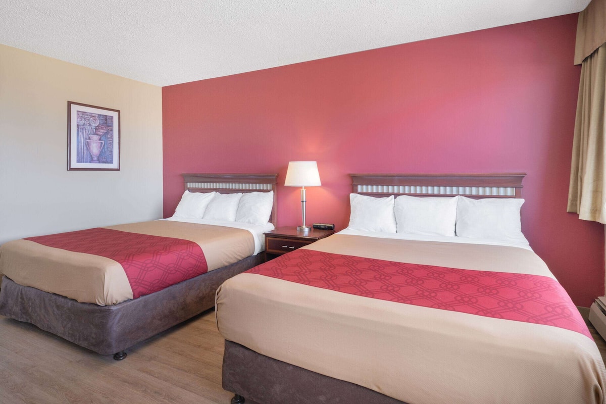 Habitación de hotel con dos camas, una mesita de noche, una lámpara y un cuadro en la pared.