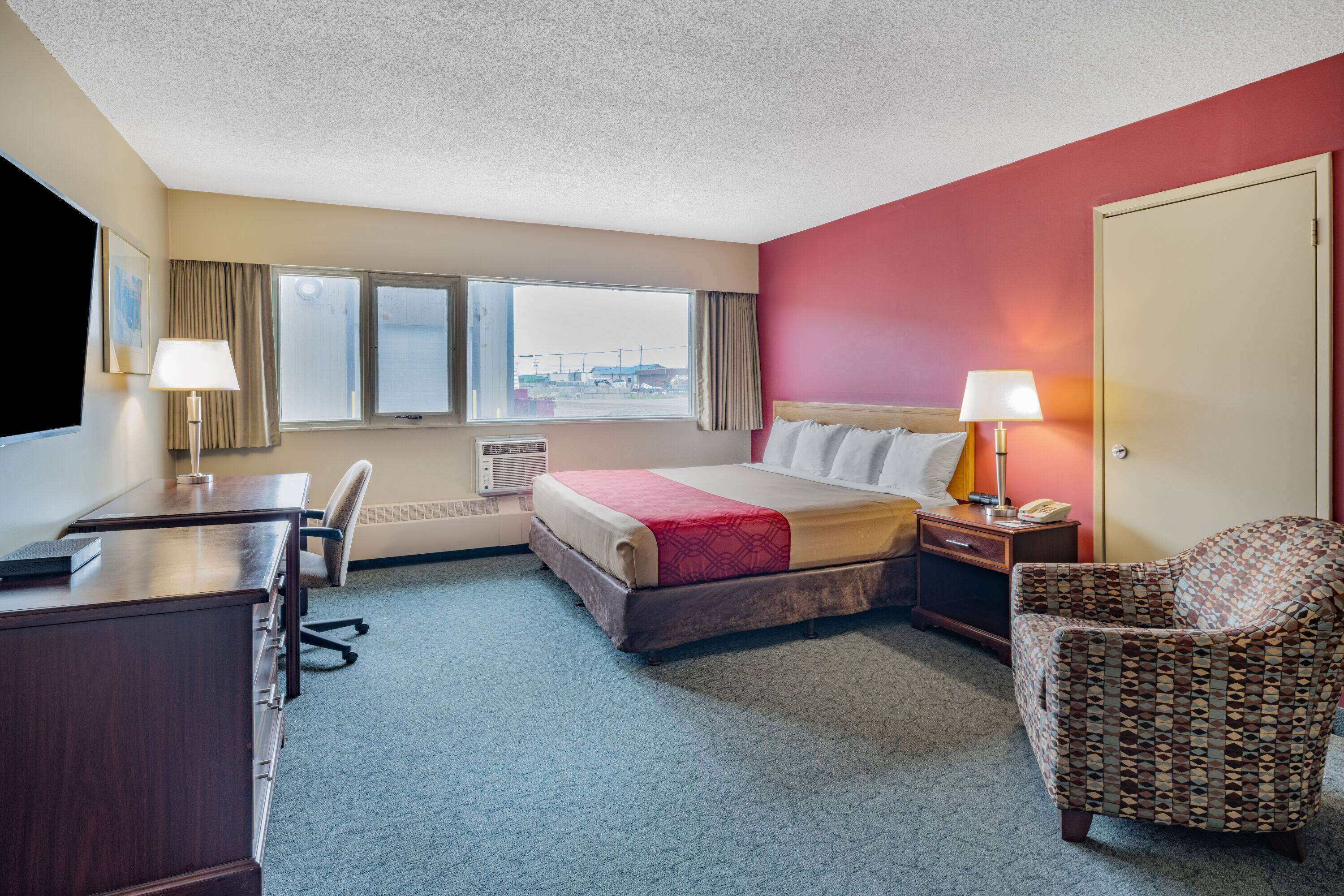 A hotel room with a bed, desk, chair, and a view of the outside.