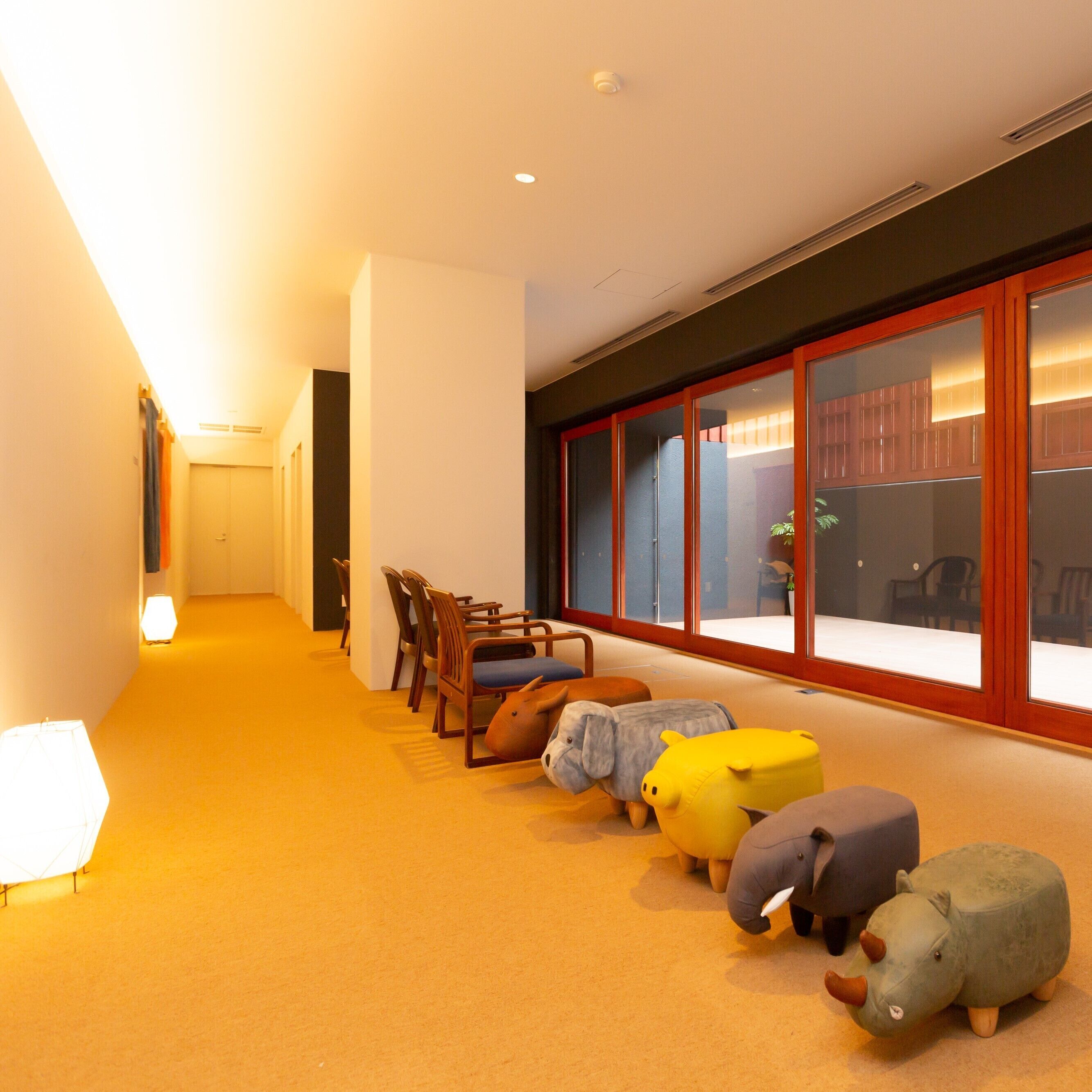 A hallway with a row of plush animal-shaped cushions, wooden chairs, and a lamp.