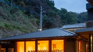 Un edificio con terraza de madera y un amplio espacio abierto con mesas y sillas, rodeado de árboles y colinas.