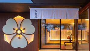 Entrada de un edificio con un gran diseño floral iluminado en la pared, puerta corredera de vidrio y un pequeño área de estar al aire libre con una planta en maceta.