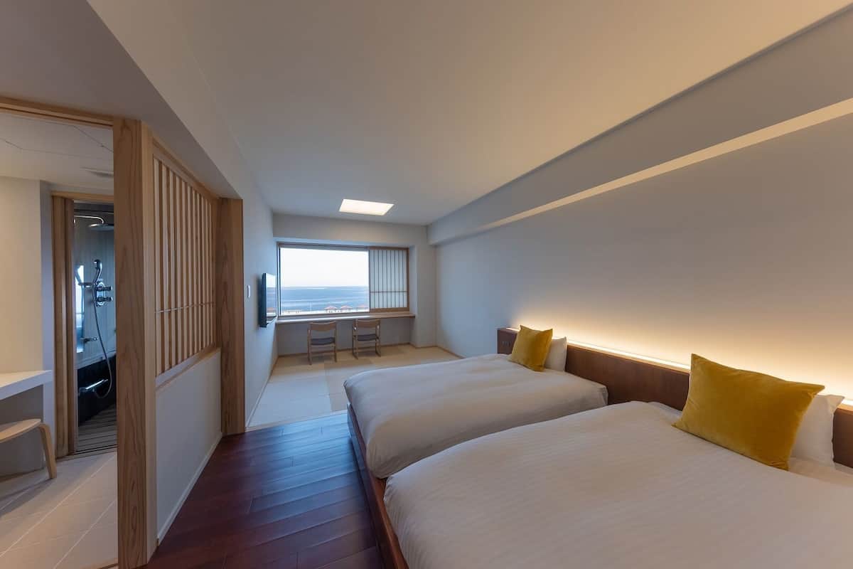 Habitación de hotel con dos camas, un escritorio pequeño, una ventana con vistas y zona de ducha.