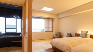 Habitación de hotel moderna con una cama grande, zona de estar con vistas y puerta corredera que da a un balcón.