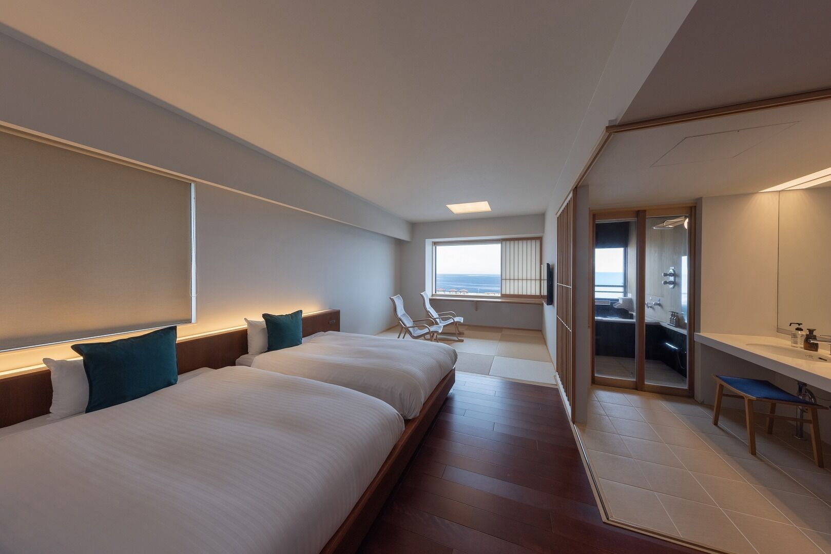 Habitación de hotel con dos camas, un escritorio, una silla, un espejo grande y vistas al mar.