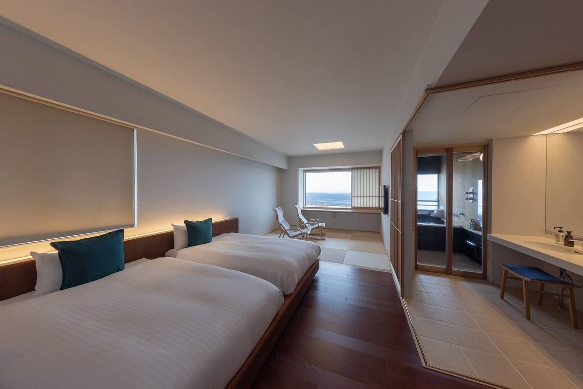 Habitación de hotel con dos camas, un escritorio, una silla, un espejo grande y vistas al mar.