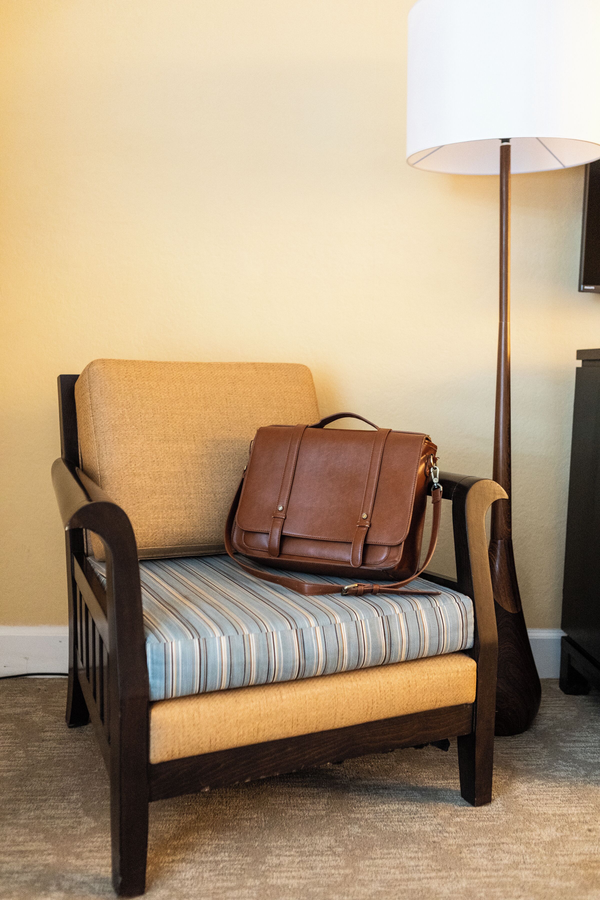 A chair with a striped cushion and a brown leather bag placed on it.