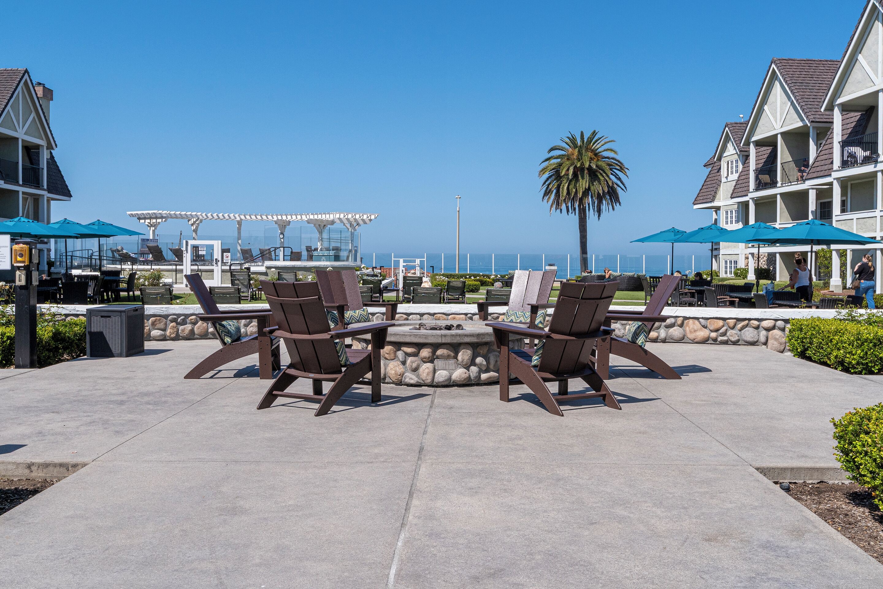 An outdoor patio with lounge chairs, a fire pit, and umbrellas.