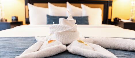 A neatly made bed with a towel arrangement in the shape of a star, a headboard, and a bedside table with a lamp.