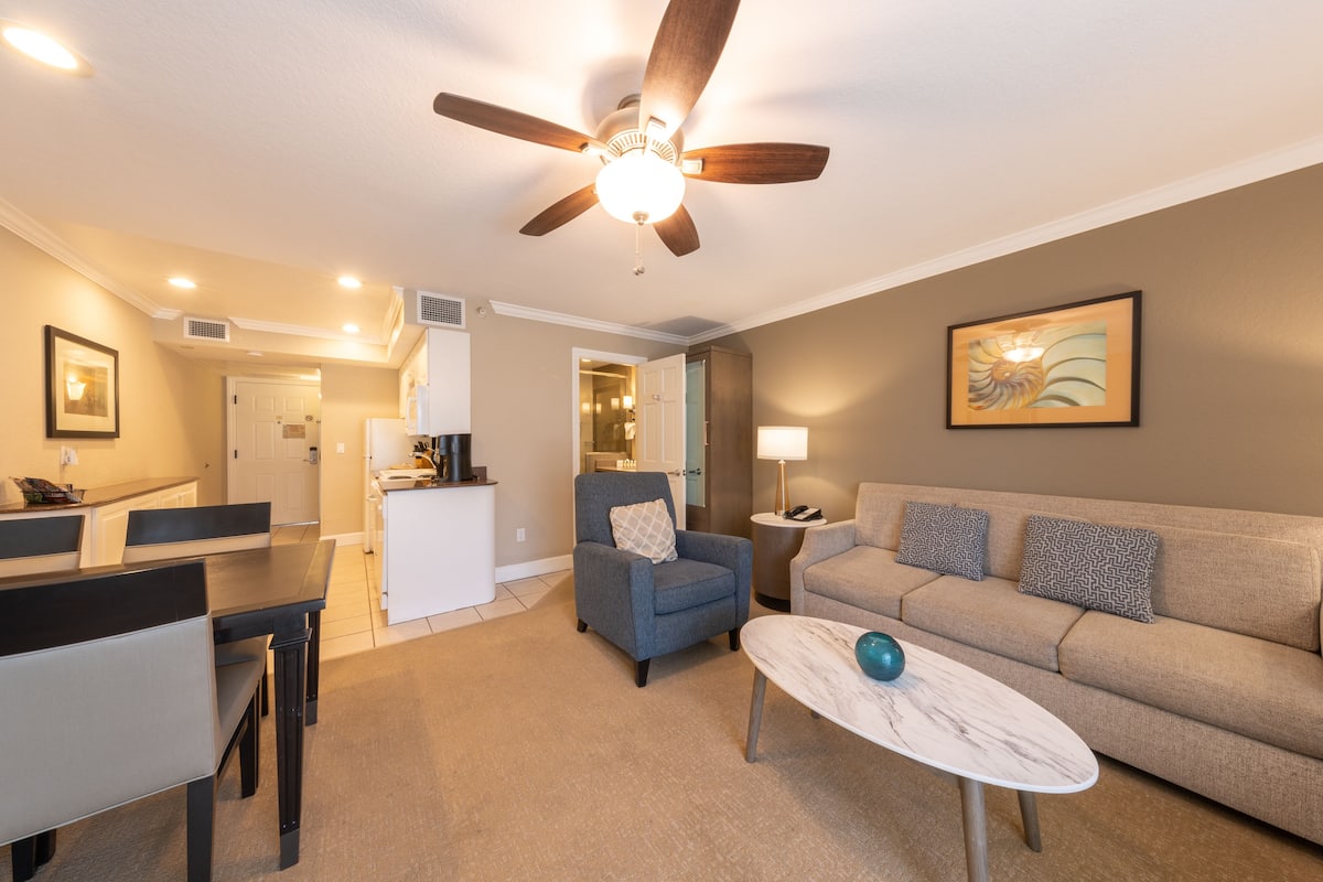 A modern living room with a ceiling fan, a sofa, a coffee table, and a dining area with a table and chairs.