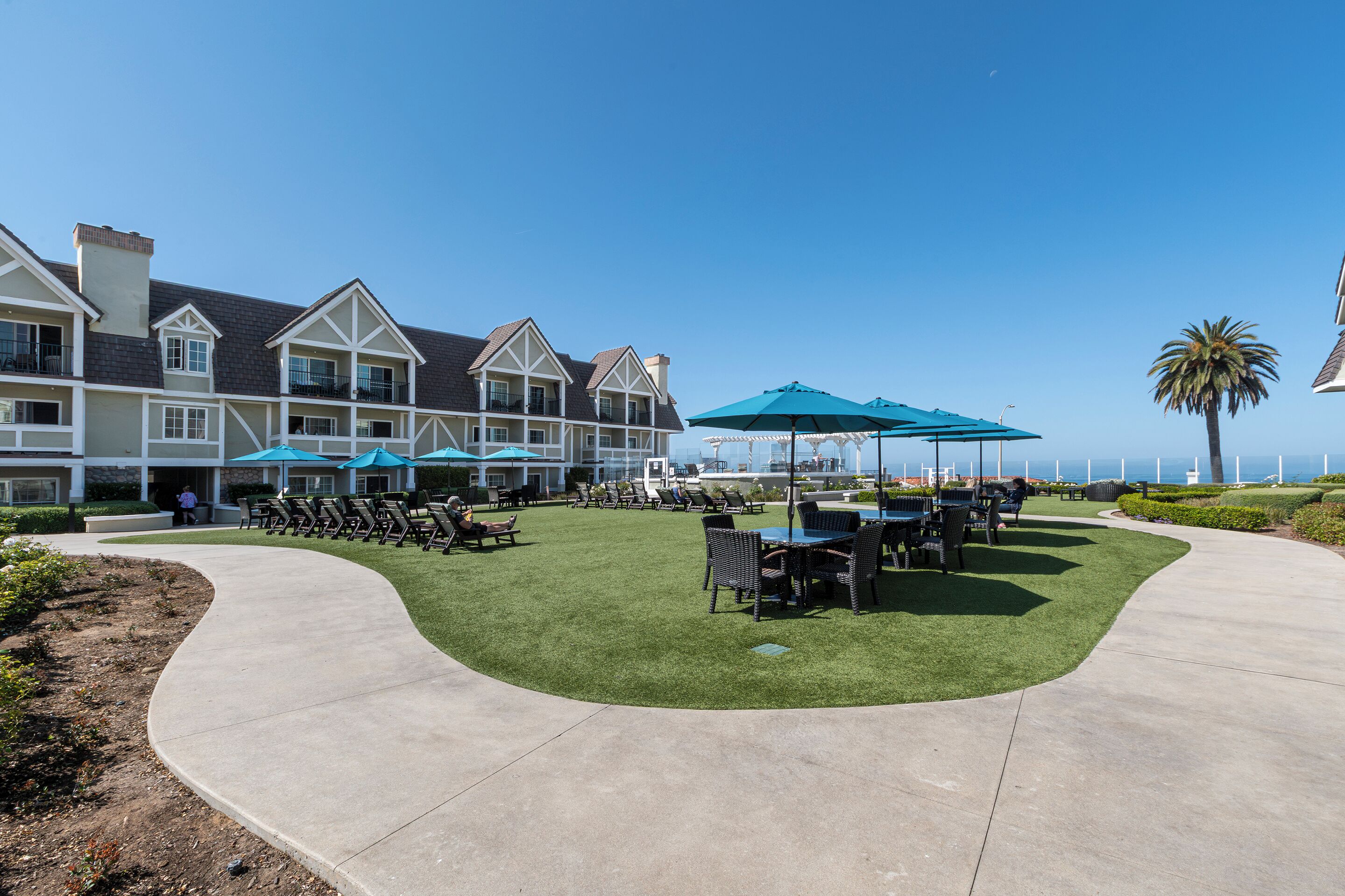 A resort with outdoor seating, a pool, and a view of the ocean.