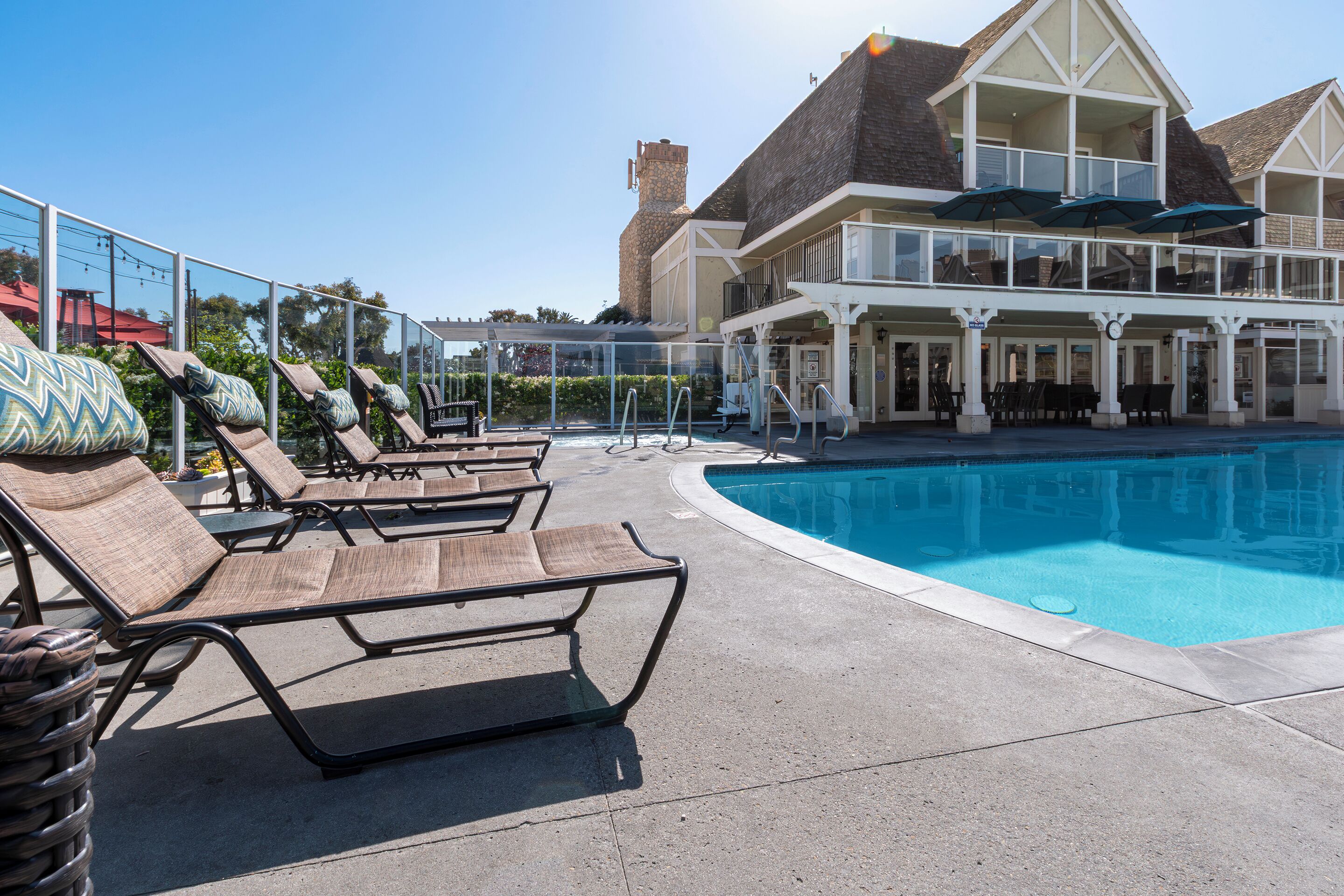 A poolside area with lounge chairs and umbrellas, a clear blue pool, and a building with a balcony.
