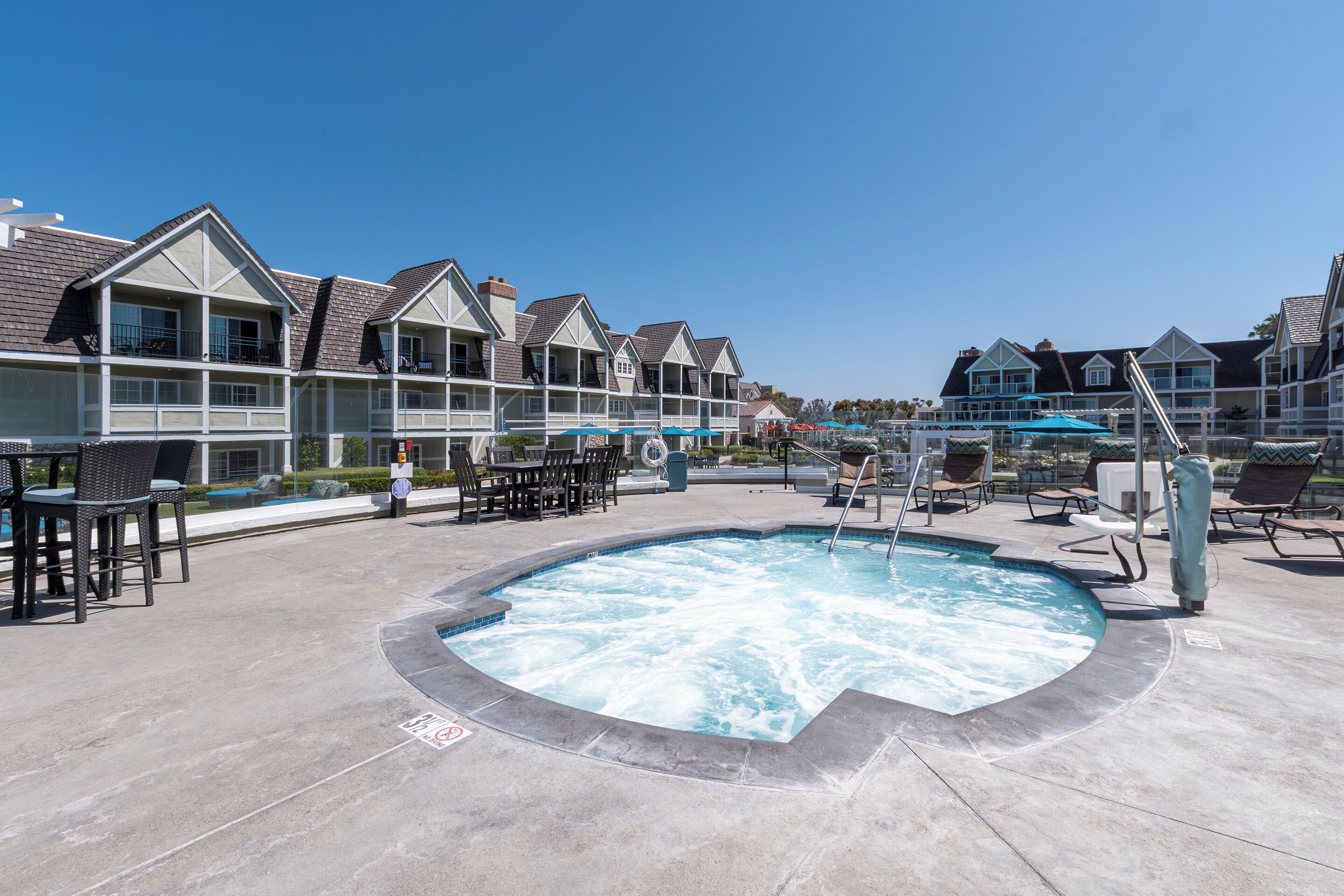 A swimming pool with lounge chairs and umbrellas, surrounded by multi-story buildings with balconies.