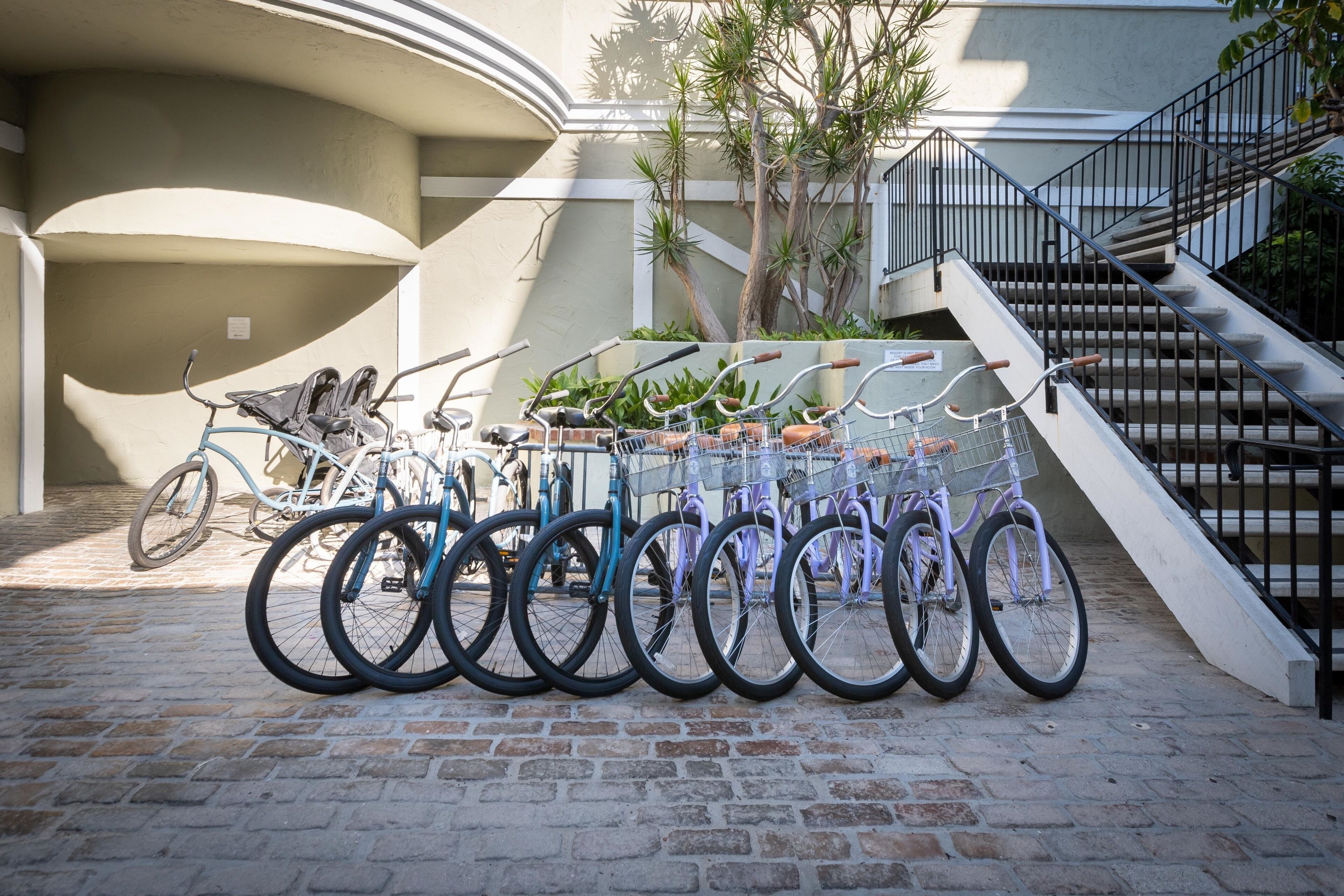 A row of bicycles parked on a cobblestone path with a staircase and greenery in the background.