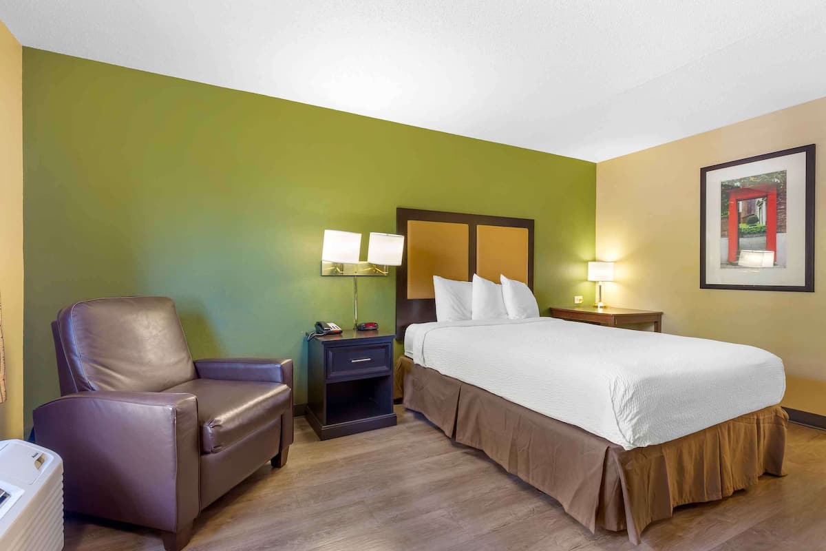 Ein Hotelzimmer mit einem Bett, einem Sessel, einem Nachttisch und einer Wandlampe.
