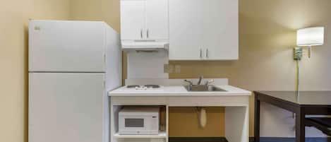 A compact kitchen with white cabinets, a built-in microwave, a sink, and a refrigerator.