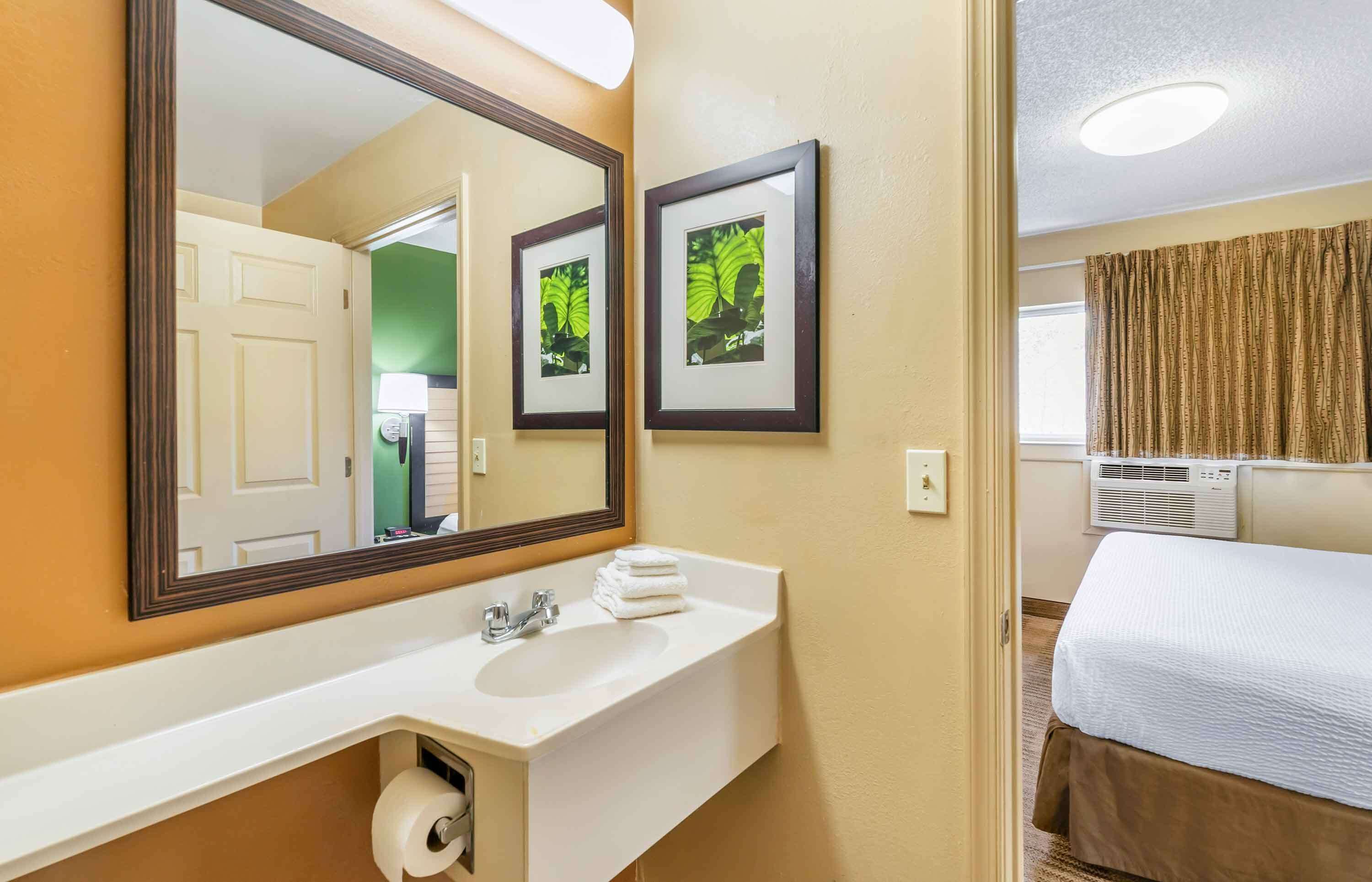 Hotellin kylpyhuone, jossa on pesuallas, peili ja seinällä kehyksiin kiinnitetyt taulut.