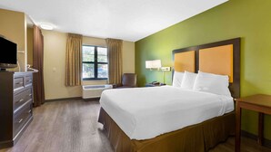 Ein Hotelzimmer mit Bett, Schreibtisch, Stuhl, Fernseher und einem Fenster mit Vorhängen.