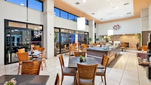 Un comedor espacioso con varias mesas y sillas, ventanas amplias y una zona de cocina con mostrador.