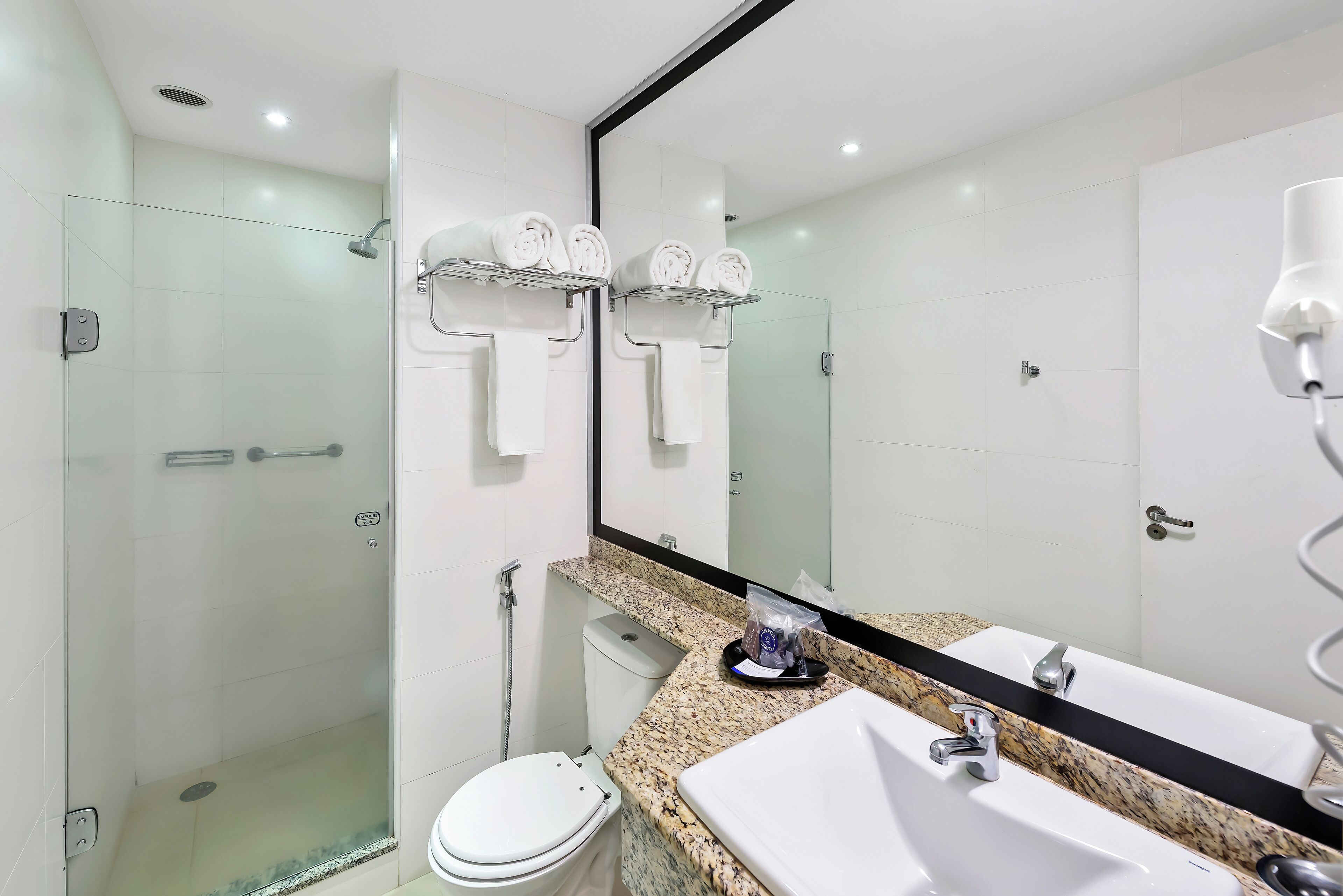 Uma casa de banho moderna com chuveiro envidraçado, sanita, lavatório com bancada de granito e um espelho grande.