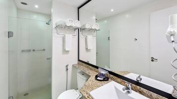 Uma casa de banho moderna com chuveiro envidraçado, sanita, lavatório com bancada de granito e um espelho grande.
