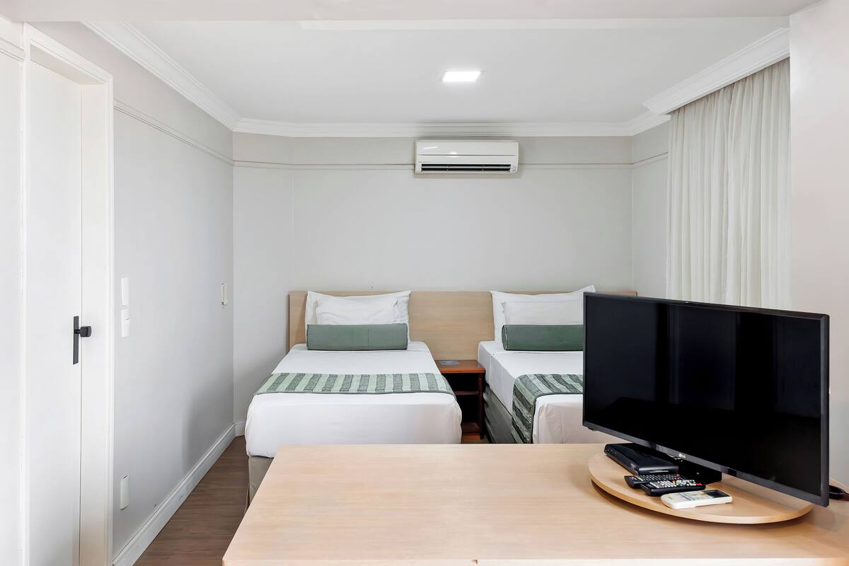 Habitación de hotel con dos camas, un televisor y un escritorio con control remoto.