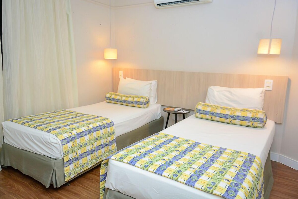 Habitación de hotel con dos camas, cada una con una colcha estampada, una mesita de noche y un aire acondicionado de pared.