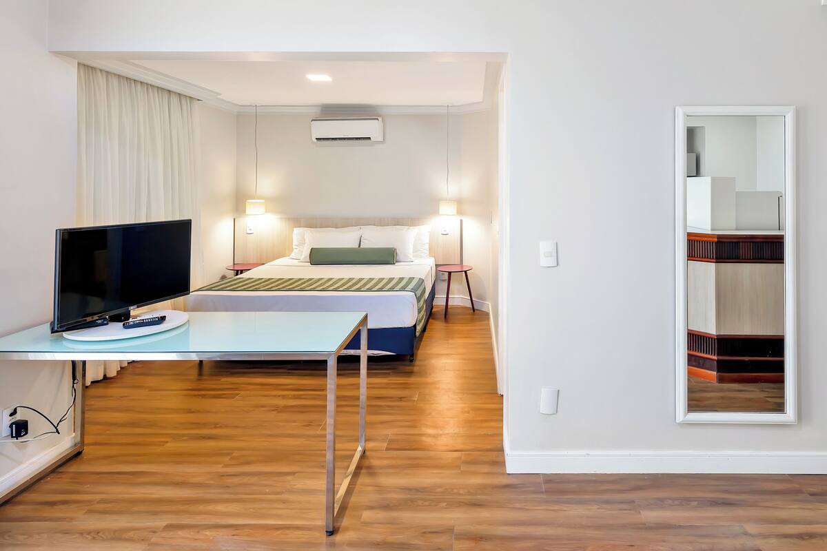Una habitación de hotel con una cama, lámparas de noche, televisión y escritorio.