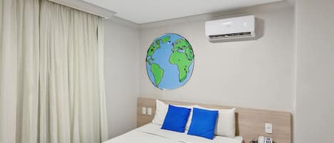A hotel room with a bed, a round wall decoration of the Earth, an air conditioning unit, a bedside table with a phone, and a curtain.