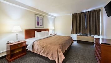A hotel room with a bed, bedside lamps, a nightstand, a dresser, a flat-screen TV, and a window with curtains.