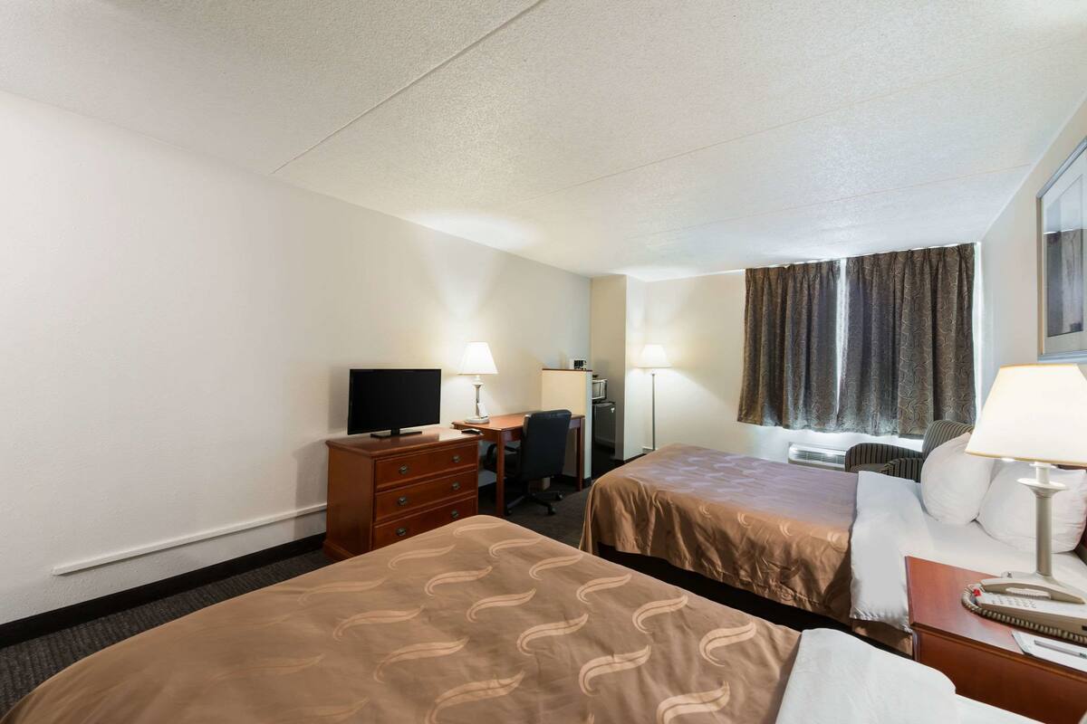 A hotel room with two beds, a desk, a chair, a television, and a window with curtains.