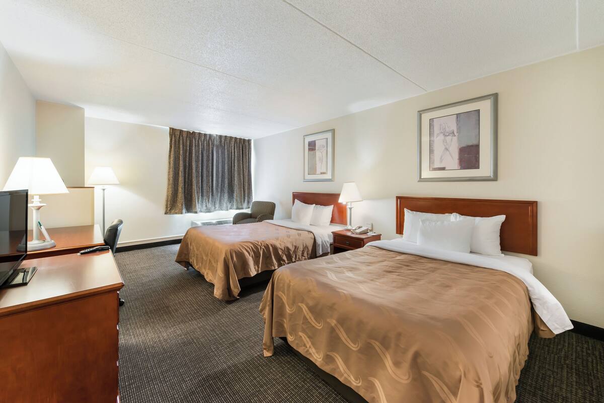 A hotel room with two beds, a desk, a chair, and a TV.