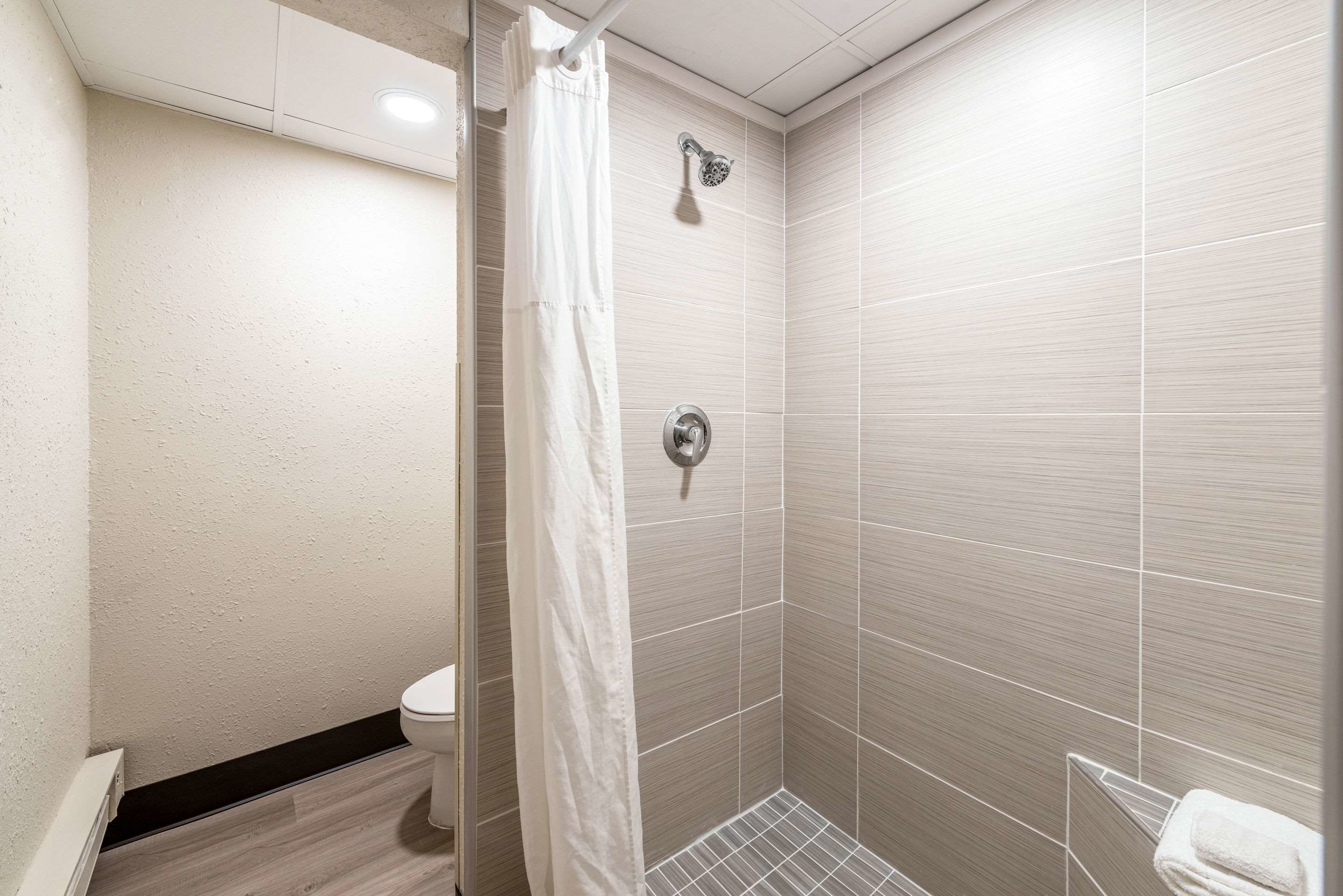 A small, modern bathroom with a shower, toilet, and a towel rack.
